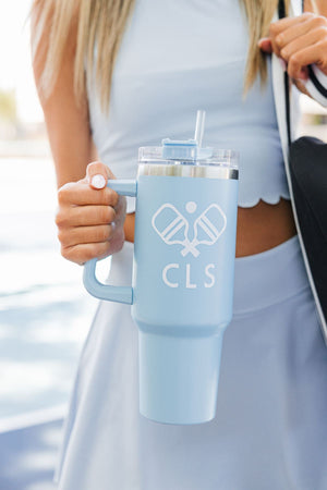 A girl in a blue outfit holds up a blue 40 oz tumbler with a white pickleball and monogram design
