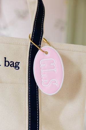 Pink oval bag tag with CLS hanging off of a canvas tote bag.