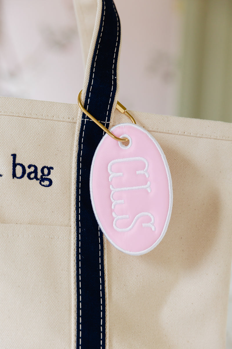 Pink oval bag tag with CLS hanging off of a canvas tote bag.