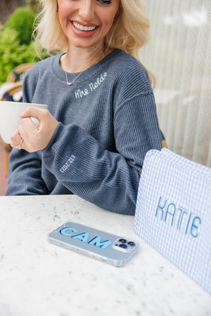 A woman holds a coffee cup while wearing a navy corded sweatshirt which is personalized with "Mrs. Fields" on the collar and custom wedding date on the sleeve.
