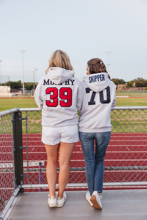 Two gray embroidered gameday hoodies with appliquéd player names and numbers “Murphy 39” and “Skipper 70”