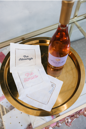 An assortment of embroidered cocktail napkins customized with last names next to a bottle of wine.