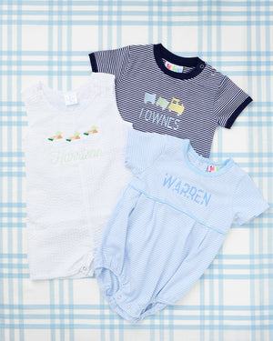 Short Sleeve Striped Bubbles from Rainey Laine featuring personalized designs—light blue striped bubble with a green tractor trailer motif and name ‘Henry,’ and navy striped bubble with yellow construction truck motif and name ‘Townes,’ both laid out on a soft blue plaid background.