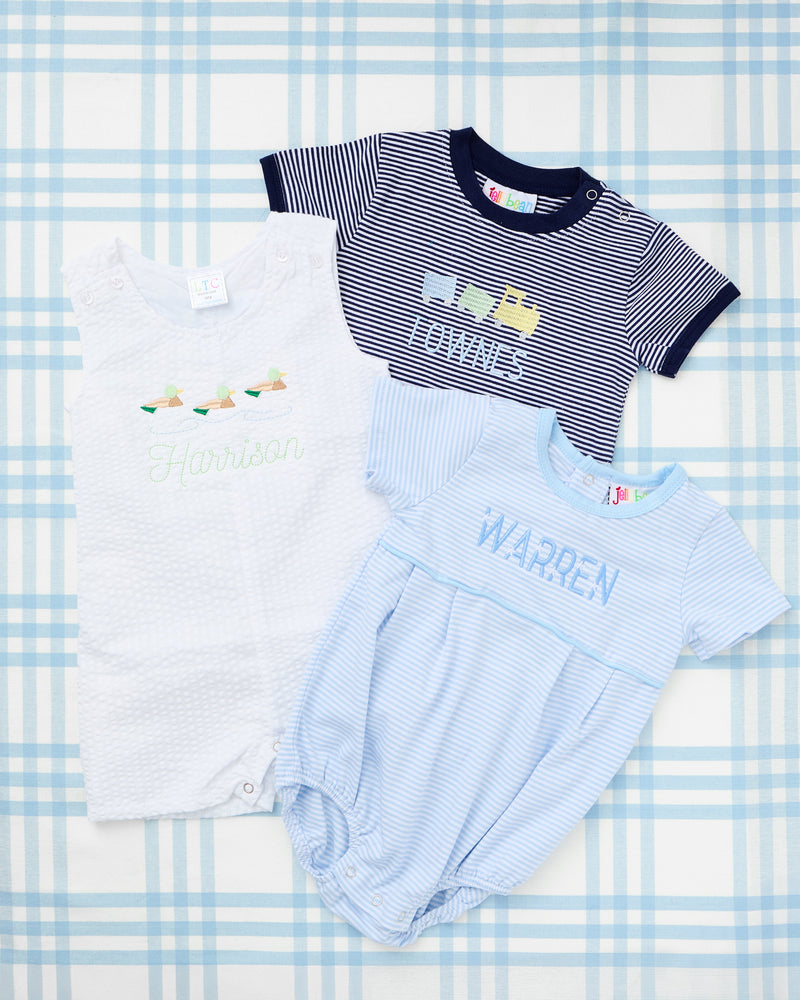 Short Sleeve Striped Bubbles from Rainey Laine featuring personalized designs—light blue striped bubble with a green tractor trailer motif and name ‘Henry,’ and navy striped bubble with yellow construction truck motif and name ‘Townes,’ both laid out on a soft blue plaid background.