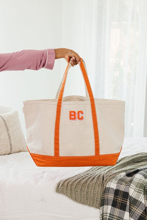 A person holds up an orange canvas tote with a pink and orange monogram.