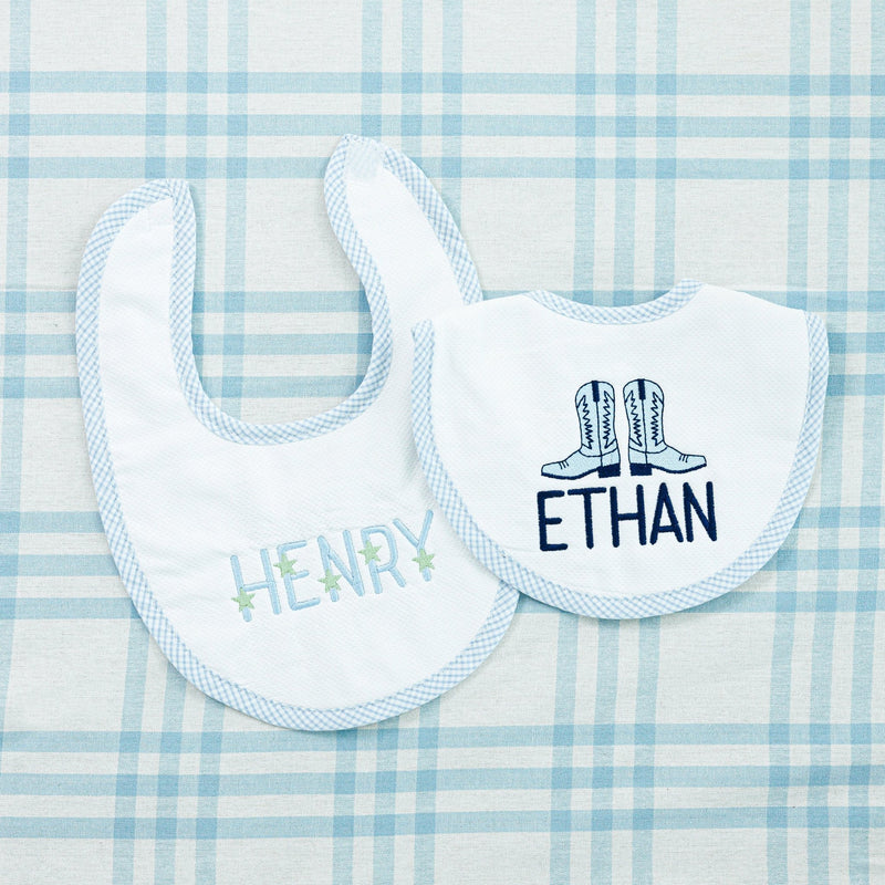 Two personalized baby bibs on a blue checkered fabric background