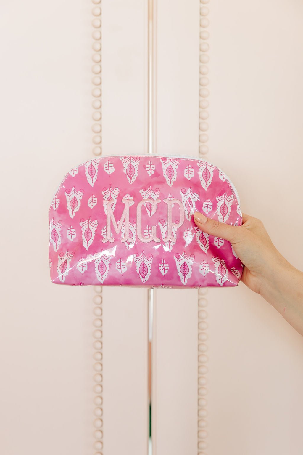 Three clear-coated pouches: a pink block-print rectangular pouch monogrammed 'AHR', a green leopard dome pouch monogrammed 'EGB', and a blue floral pouch monogrammed 'CBR'