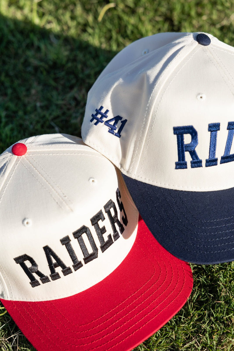 Cream vintage trucker hats: red-brim “RAIDERS” and navy-brim “#41 RILEY,” highlighting the Custom Collegiate Vintage Trucker Hat.
