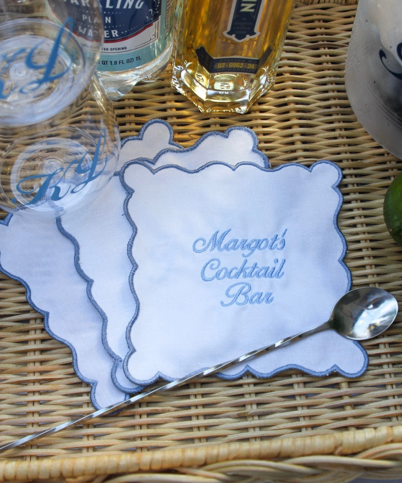 White cocktail napkins with scalloped edges, embroidered with “Margot’s Cocktail Bar” in blue and “The Browns” in pink.