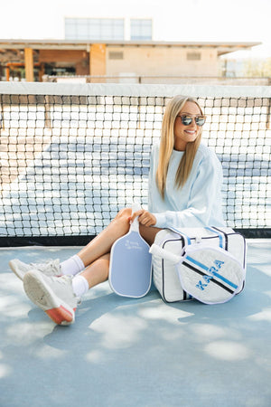 A girl sits on a pickleball court with her customized pickleball sweatshirt and gear