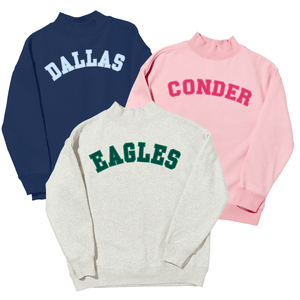 Three mockneck sweatshirts appliqued with 'Dallas' in white on navy, 'Conder' in pink on light pink, and 'Eagles' in green on heather gray.