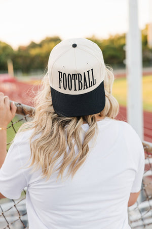 Back view of woman in backward cream-black “FOOTBALL” cap at stadium