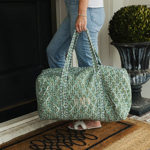 Green embroidered block print duffel with custom initials, carried for weekend travel.