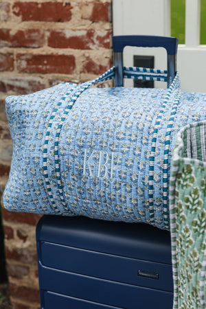 Blue Embroidered Block Print Duffel bag with white monogram resting on navy suitcase, stylish travel essential.
