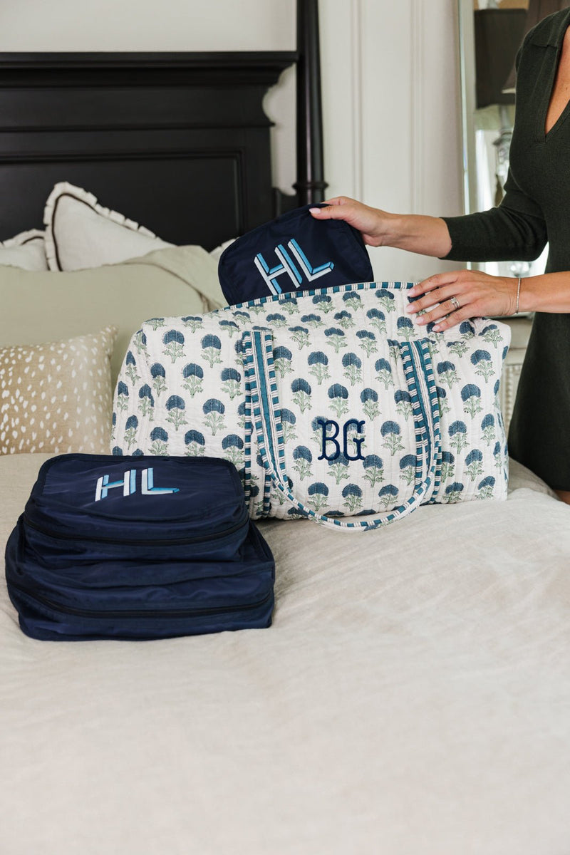 White and blue Embroidered Block Print Duffel with monogram, styled with navy packing cubes on bed