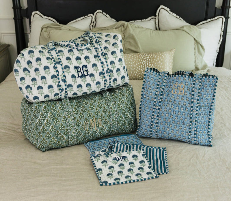 Personalized embroidered block print duffel and tote bag set in blue and green patterns, styled on a bed.