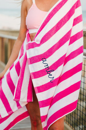 A girl wraps herself in a pink cabana towel with her name embroidered on it in a navy blue thread.