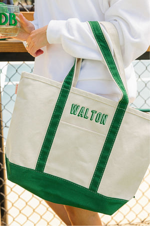 A girl holds up a green canvas tote with a green last name embroidered on it.