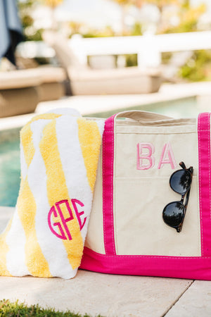 A pink canvas tote is customized with a pink monogram and holds a yellow cabana towel with a pink circle monogram.