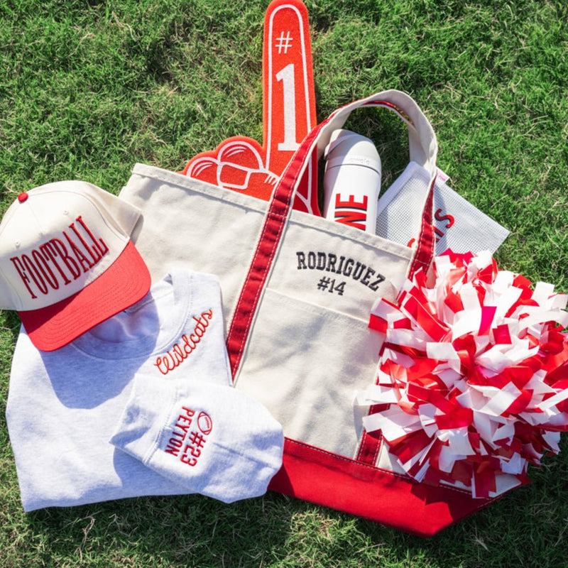 Collection of sports-themed items including a cap, bag, and pom-poms on grass.