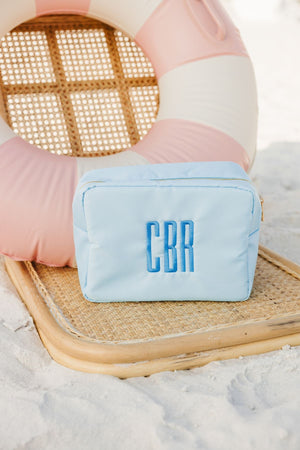 A light blue nylon pouch is customized with a blue monogram at the beach.