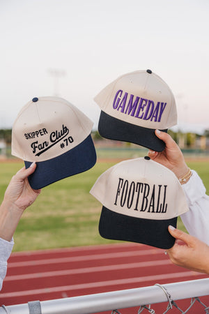 Hands display an Embroidered Fan Club Vintage Trucker Hat alongside Gameday lids on the bleachers.
