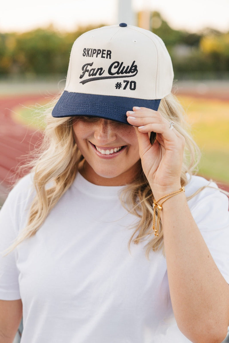 Smiling fan tips a navy-brim Embroidered Fan Club Vintage Trucker Hat reading “Skipper Fan Club #70.”