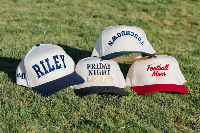Hat lineup on grass, center cap embroidered featuring “Friday Night Lights”.