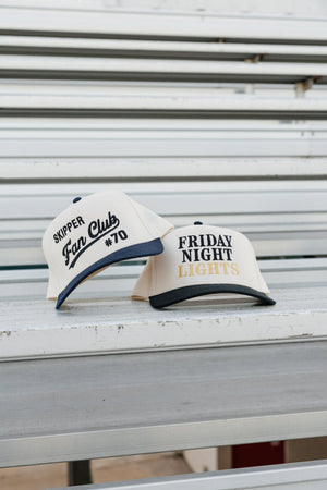 Two embroidered caps, Fan Club and Friday Night Lights, on bleachers.