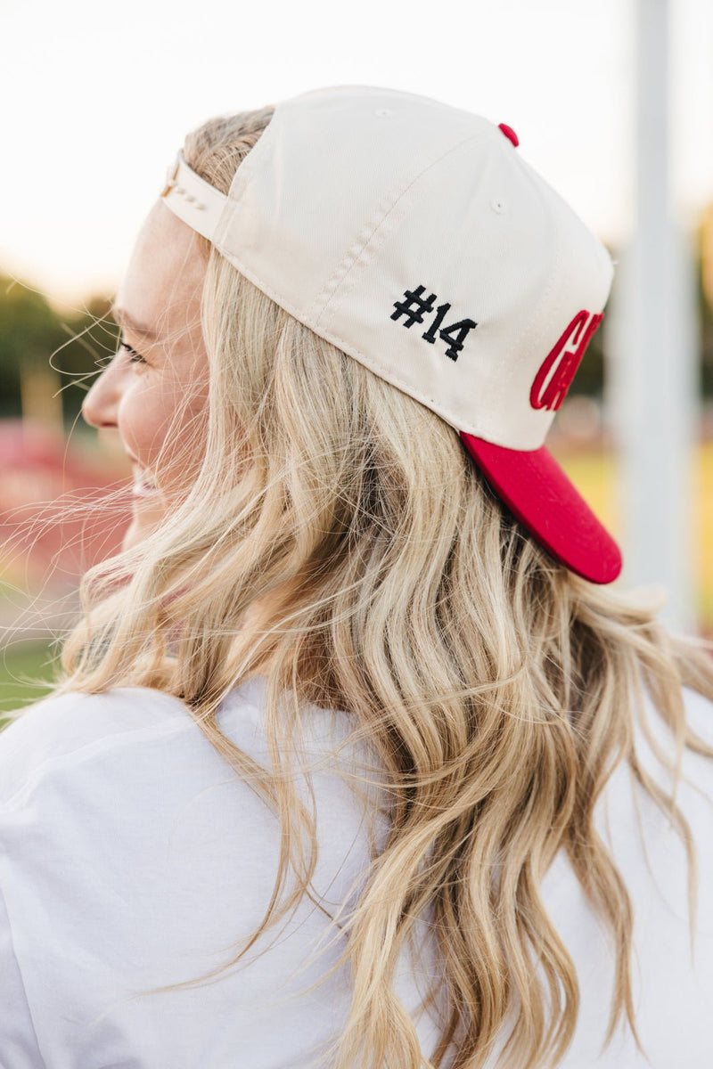 Woman in red-brim cap at bleachers, FNL embroidery.