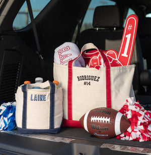 Trunk loaded with a large cream canvas tote featuring red trim and “Rodriguez #14” embroidery, plus a smaller navy-trimmed “Laine” tote.