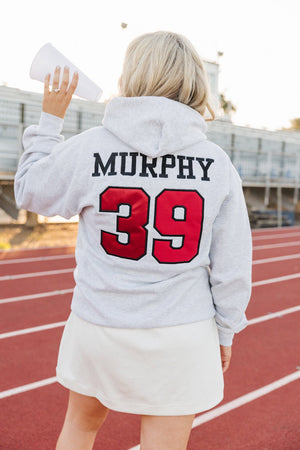 Person wearing a gray hoodie with 'MURPHY 39' printed on the back, standing on a track.