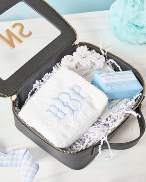 A black clear case is laid open showing a monogrammed towel and a flower hair clip.