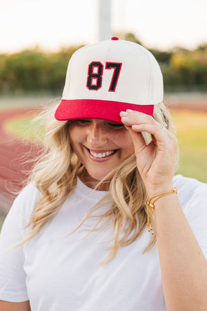 Smiling fan tips a red-brim “87” Embroidered Jersey Number Vintage Trucker Hat on the track.