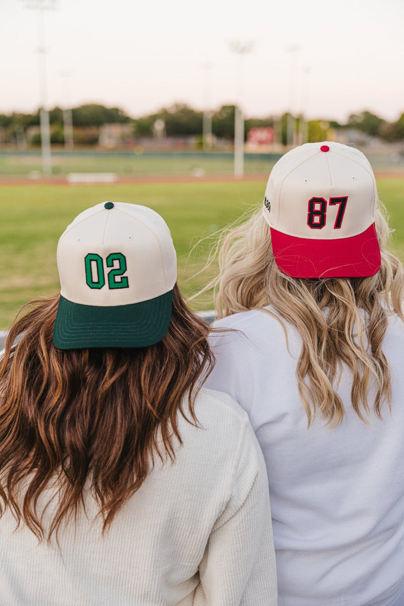 Two fans in number caps, green-brim “02” and red-brim “87”, wearing Embroidered Jersey Number Vintage Trucker Hats.