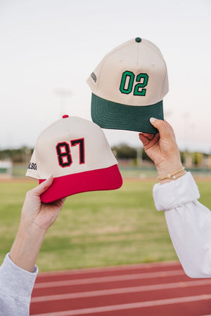 Hands holding cream caps, “02” and “87”, showcasing Embroidered Jersey Number Vintage Trucker Hat details.
