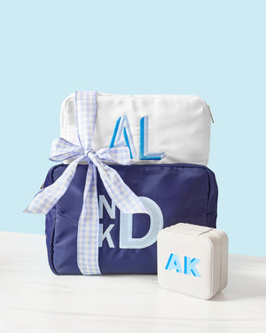 A monogrammed navy nylon pouch and a white nylon pouch are tied together and placed with a white jewelry case.
