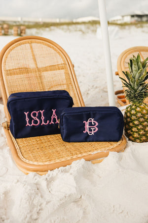 A set of navy nylon pouches are customized with a pink embroidered name and monogram at the beach.