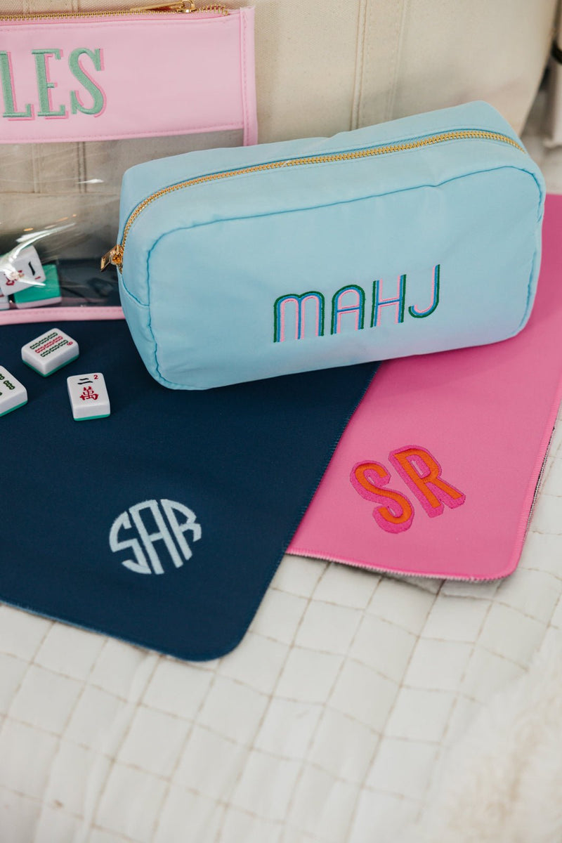 Mahjong accessories displayed with embroidered monogram tile mats in pink and navy.