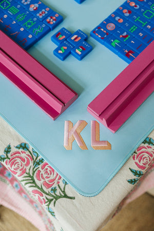 Blue embroidered mahjong tile mat with pink racks and gold monogram KL.