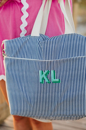 A person holds a blue striped cooler tote with a green monogram embroidered on it.