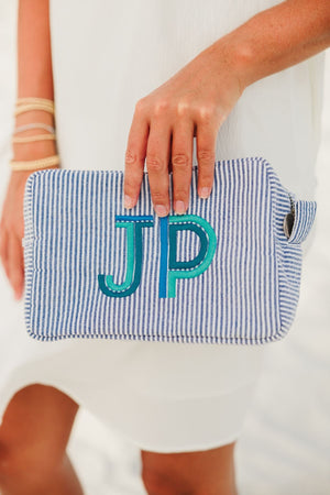 A person holds their navy seersucker pouch with a mint and turquoise embroidered monogram.