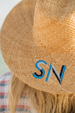 A straw hat is embroidered with a blue monogram.