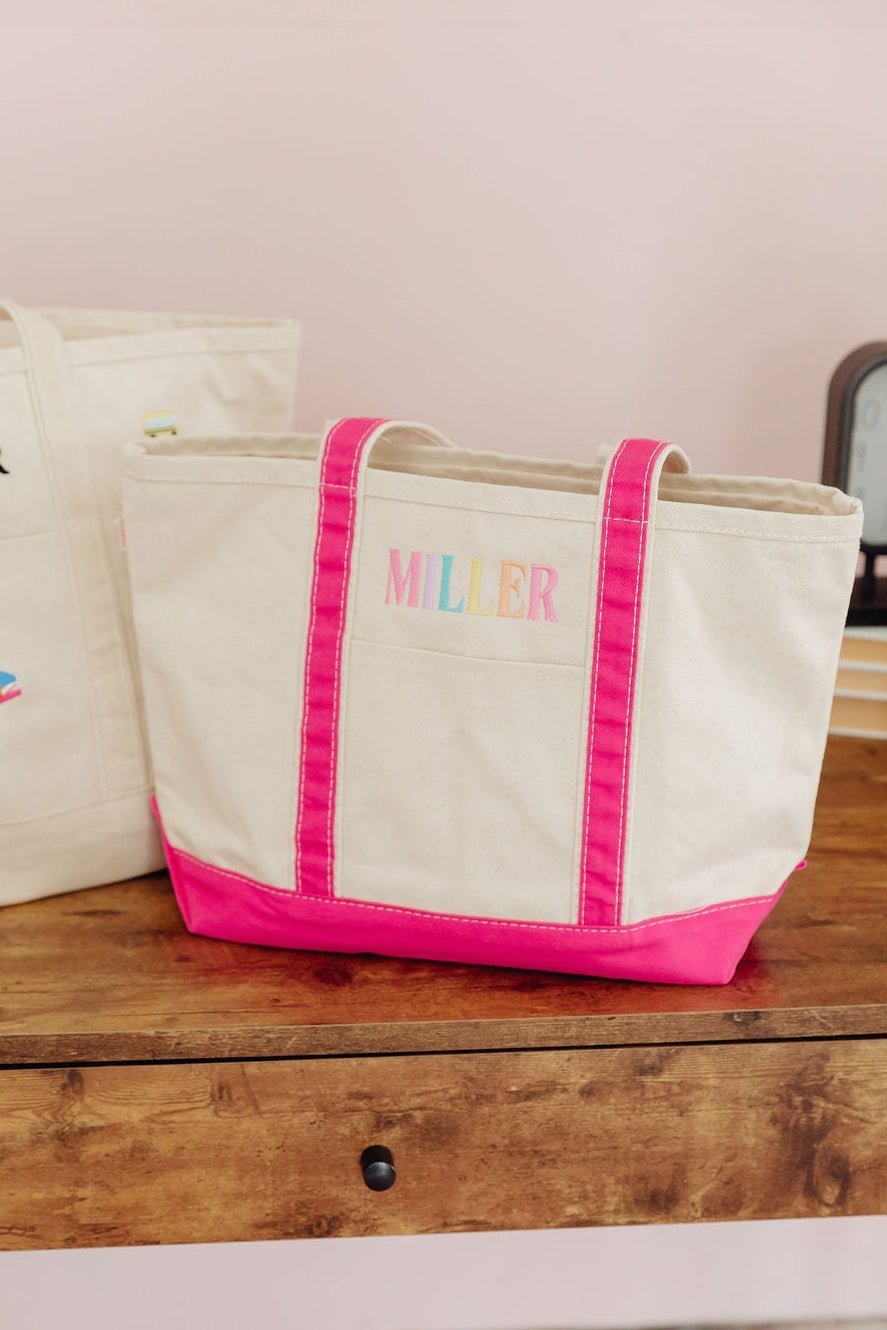 Three natural canvas totes with colorful embroidered names 'Jones' in orange trim, 'Conder' in pink trim, and 'Brown' in white trim