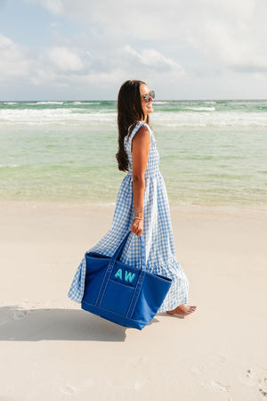 A girl walks along the water at the beach with her monogrammed blue coated canvas tote