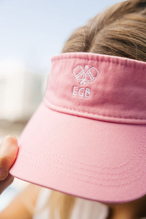 A girl wears a pink visor with an embroidered pickleball motif and her initials