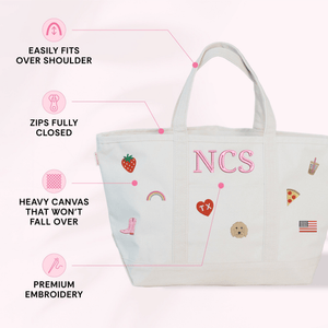 Diagram of a natural canvas tote monogrammed 'NCS' with embroidered icon patches, calling out features: easily fits over shoulder, zips fully closed, heavy canvas that won't fall over, and premium embroidery