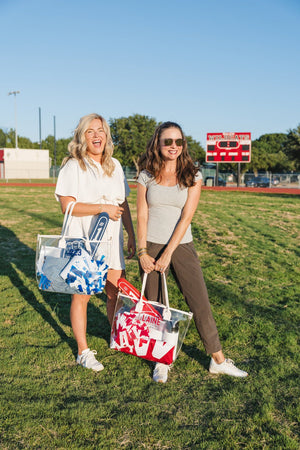 Two friends on the field carry Gameday Clear Tote Bags, blue and red sets, each customized for gameday spirit.