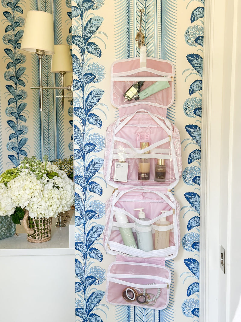 Hanging embroidered pink toiletry bag from Sprinkled With Pink, filled with beauty and skincare essentials.