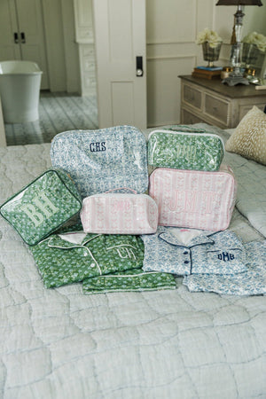 Assorted green, pink, and blue monogrammed hanging toiletry bags paired with matching pajamas displayed on bed.